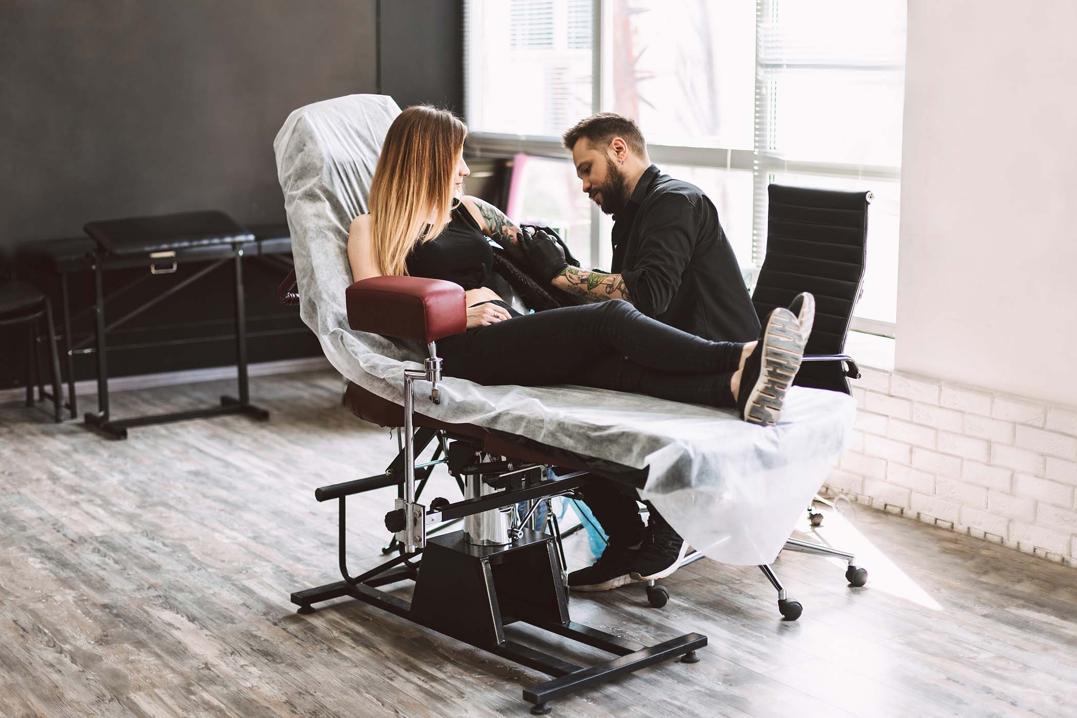 Professional tattooer carefully doing tattoo on girl hand using tattoo machine in modern tattoo studio